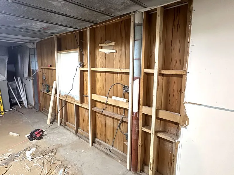 Basement wall stripped back to studs and original plank sheathing after cabinets were removed