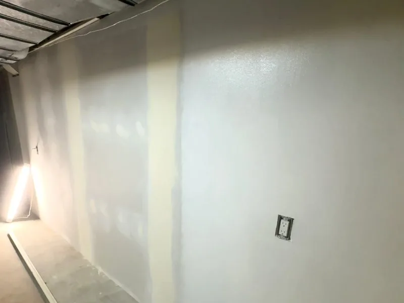 New drywall hung on the basement wall with seams taped and coated in joint compound
