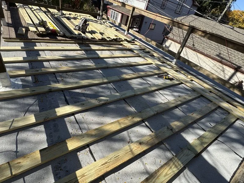 Pressure-treated sleepers laid across a garage roof before new deck boards go down