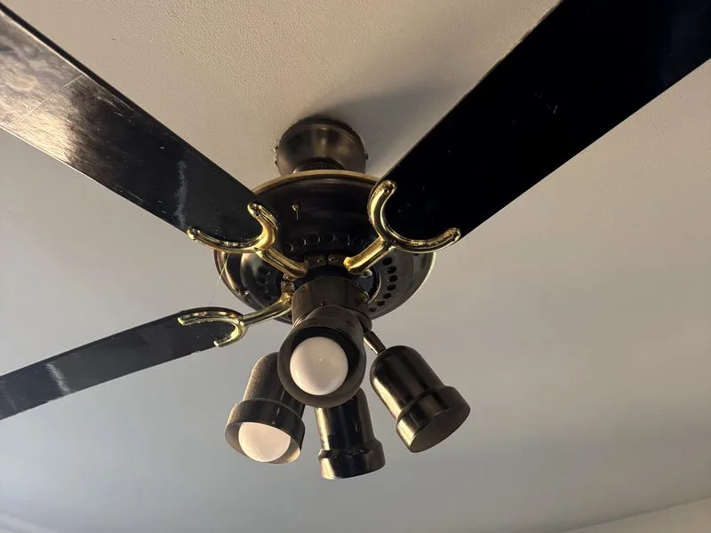 Old brass and black ceiling fan with a dated three-bulb light kit before replacement