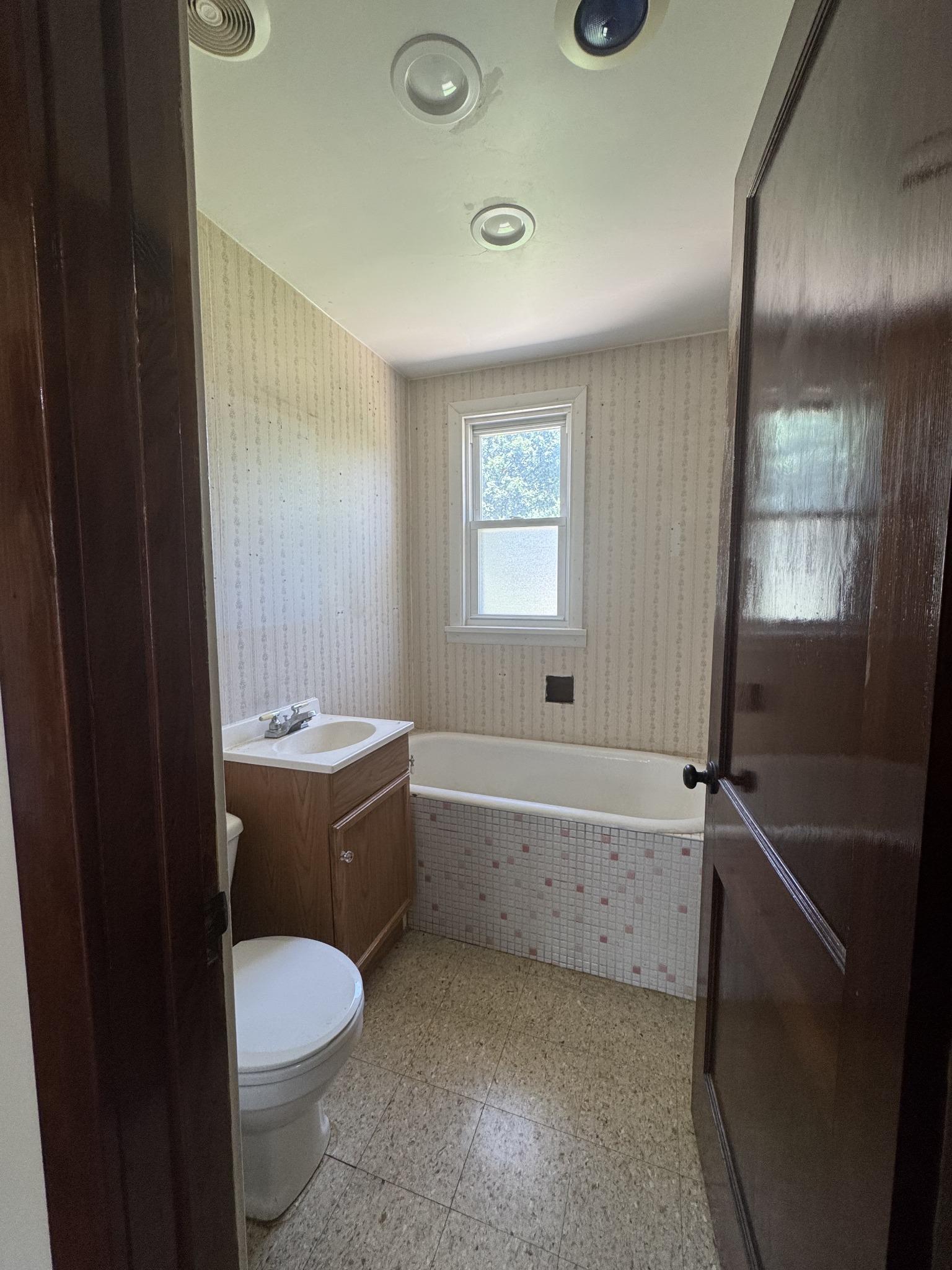 Original wallpaper, wood vanity and mosaic tub surround. Bathroom remodeling project in Joliet, Illinois.