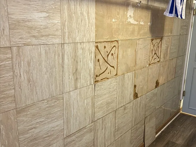 Laundry room wall with peel-and-stick tile partially removed, showing dried adhesive residue underneath